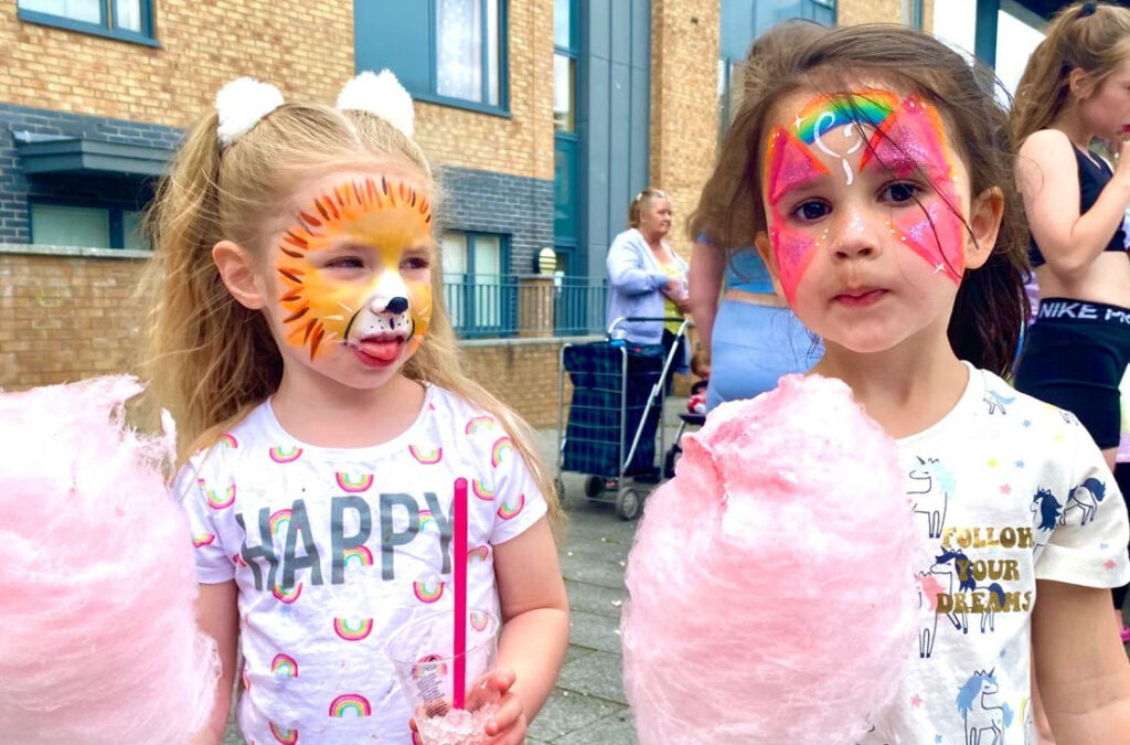 2 children, both female with face painting on their face holding cotton candy.